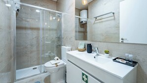 Ein modernes Badezimmer mit einer gläsernen Duschkabine, Toilette, Waschbecken und Pflegeprodukten sowie einem Spiegel.