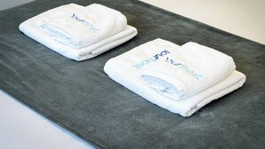 Deux serviettes blanches pliées, avec l’inscription «Jung Hotel», posées sur un tapis gris.