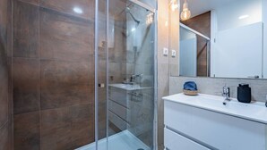 Une salle de bain moderne avec une douche à l’italienne en verre, un meuble-lavabo blanc et un grand miroir.