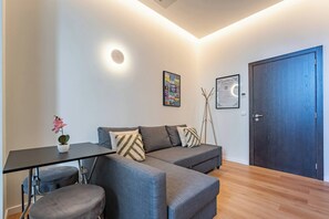 Ein modernes Wohnzimmer mit einer Couch, einem kleinen Tisch, einer Topfpflanze und einer Tür.