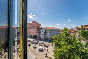 Stadtansicht mit Gebäuden, blauem Himmel und einem Baum im Vordergrund.