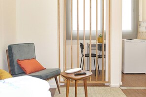 A hotel room with a bed, a chair with a cushion, a small table with a remote control, and a kitchenette area with a refrigerator. - Oporto Sweet Downtown 4 (Porto)