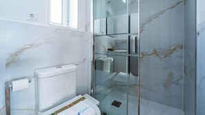 Un bagno con il water, cabina doccia in vetro e parete in marmo.