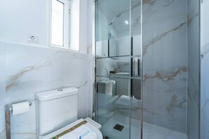 Ein Badezimmer mit Toilette, einer Duschkabine aus Glas und einer Marmorwand.