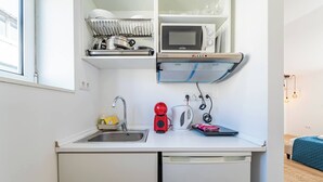 Un angolo cottura compatto con lavandino, forno a microonde, bollitore e scolapiatti.