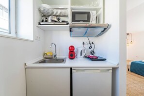 Eine kleine Küchenzeile mit Spüle, Mikrowelle, Wasserkocher und Geschirrständer.