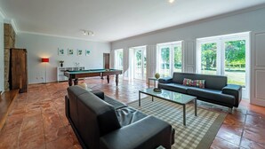 A spacious living room with a pool table, a sofa, and large windows. - Casa das Pintoras Garden and Pool (Vile)