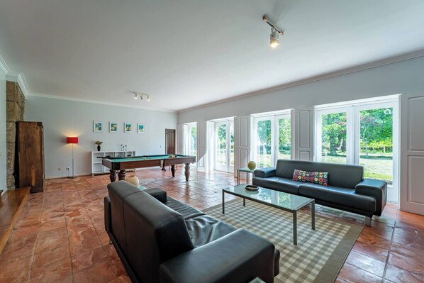 A spacious living room with a pool table, a sofa, and large windows.