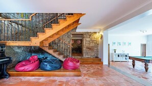 A spacious room with a wooden staircase, a stone wall, a billiards table, and a piano. - Casa das Pintoras Garden and Pool (Vile)