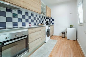 Eine kleine Küche mit Holzschränken, einem Edelstahlbackofen, einer Waschmaschine und einem kleinen Kühlschrank.