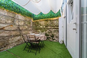 Eine Terrasse mit Tisch für zwei Personen, umgeben von Steinmauern und künstlichem Rasen.