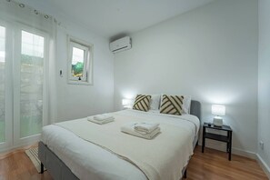 Ein Schlafzimmer mit Bett, Kissen, einem Nachttisch mit Lampe, einer Klimaanlage und einem Fenster mit Blick.