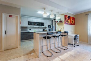 A modern kitchen with bar stools, a dining table, and a painting on the wall. - Cozy and Quiet Spacious Flat (Oliveira do Douro)