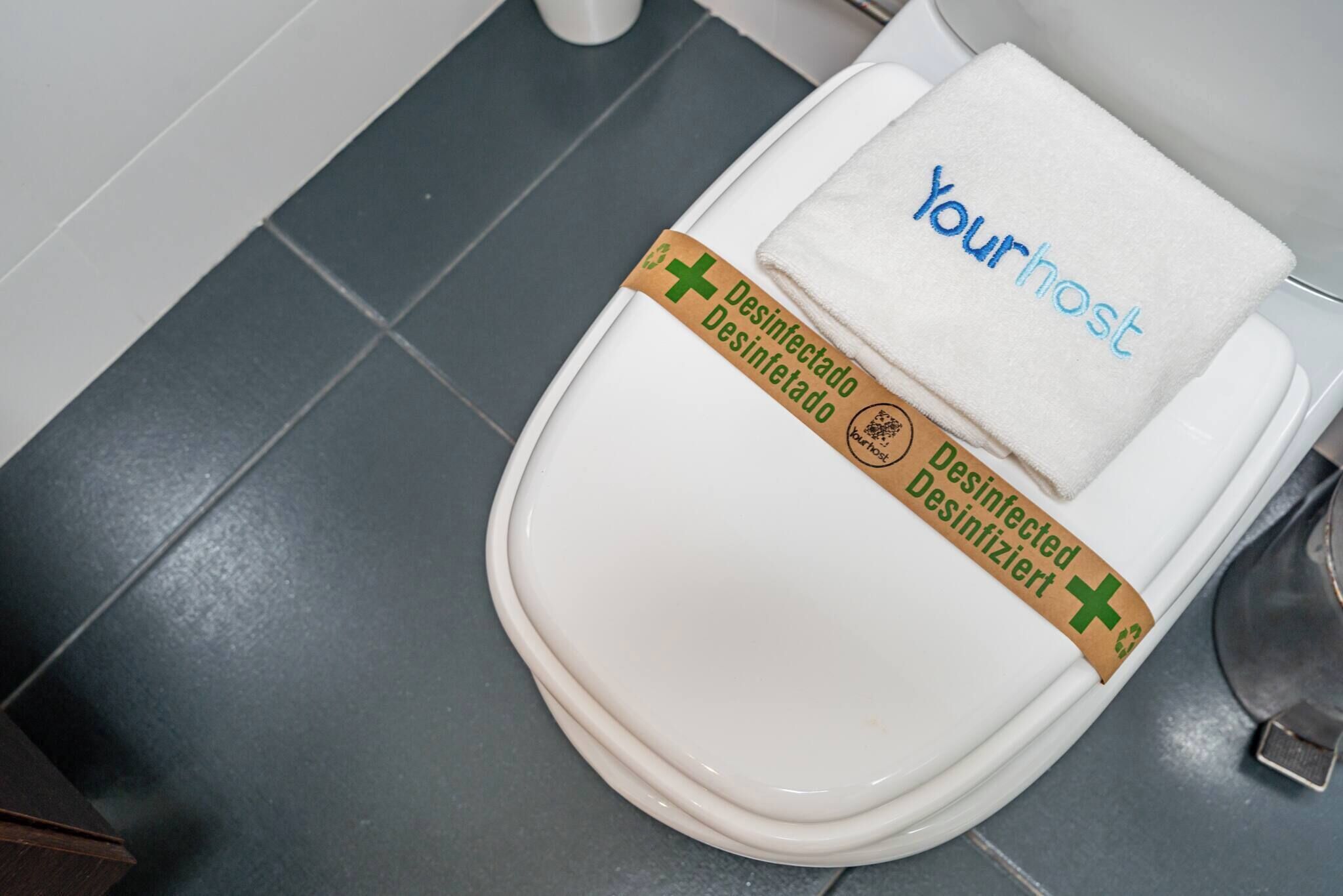 A toilet with a 'Yourhost' towel and a 'Desinfectado Desinfectado' label.