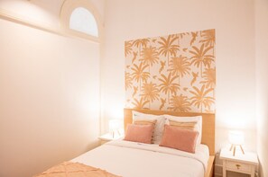 A bedroom with a bed, two bedside tables, a nightstand, a window, and a wall with a palm tree pattern. - Casa Romero - Family & Friends, Surf & Beach (Matosinhos)