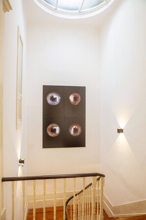 Eine Treppe mit hölzernem Geländer und weißen Spindeln, die zu einer Zwischenebene führt, auf der sich eine schwarze Kunstwerk mit kreisförmigen Mustern befindet.