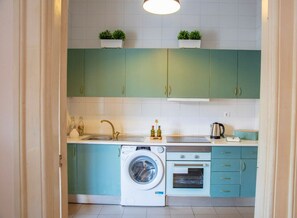 A compact kitchen with teal cabinets, a washing machine, an oven, and a sink. - Casa Romero - Family & Friends, Surf & Beach (Matosinhos)