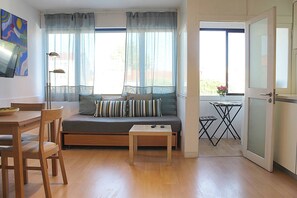 Ein Wohnzimmer mit Sofa, einem Esstisch mit Stühlen, einem kleinen Tisch und einem Fenster mit Vorhängen.