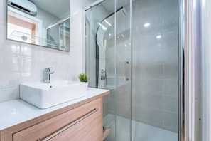 Ein modernes Badezimmer mit einer Duschkabine, einem weißen Waschbecken und einem Holzwaschtisch.