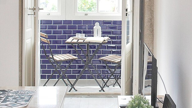 Una habitación con vistas por una ventana, una mesa con sillas y una pared de azulejos.