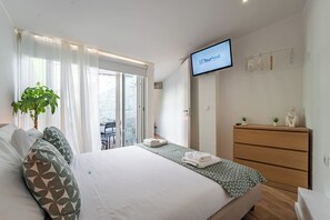 Ein Hotelzimmer mit Bett, einem an der Wand befestigten Fernseher, einer Holzkommode und einem Balkon mit Tisch und Stühlen.