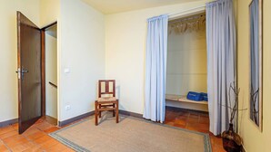 Ein Zimmer mit Holztür, einem Sessel, einem Teppich, einer Duschkabine mit Vorhängen und einem Regal mit Gegenständen.