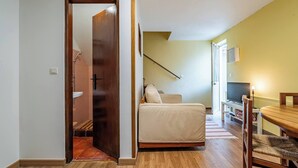 Ein Zimmer mit einem Bett, einem Holztisch, einem Fernseher und einer Treppe, die in ein weiteres Zimmer führt.