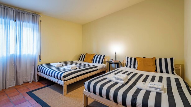 Ein Hotelzimmer mit zwei Betten, einem kleinen Tisch, einer Lampe und einem Fenster mit Vorhängen.