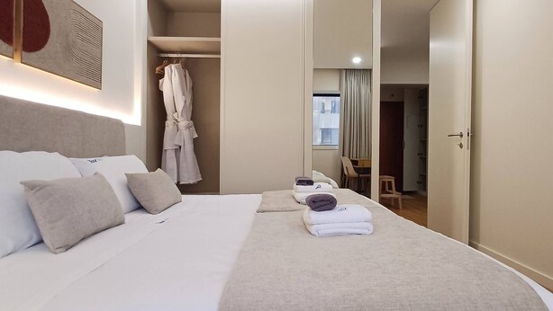 Hotellihuone, jossa on sänky, tyynyjä, naulakossa roikkuva kylpytakki ja tuoli.