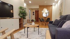 Moderni olohuone, jossa on litteänäyttöinen televisio, harmaa sohva, pieni pyöreä pöytä, ruukkukasvi ja puinen kaappi.
