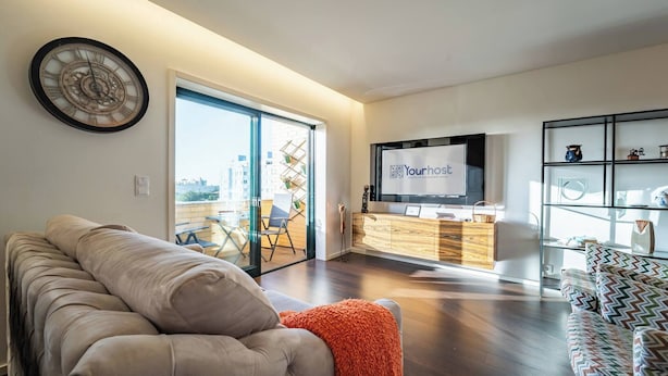 Een moderne woonkamer met een bank, een televisie en een decoratieve klok aan de muur.