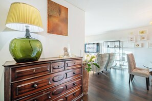 A modern living room with a wooden dresser, a green lamp, and a glass coffee table. - Beach Apartment with Comfort and Soul (São Félix da Marinha)