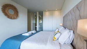 Een hotelkamer met een bed, hoofdeinde, een spiegel aan de muur en een deur naar een badkamer.