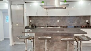 Eine moderne Küche mit einer zentralen Kochinsel, Barhocker, Edelstahlgeräten und einer Spritzschutzwand.