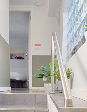 Eine Treppe mit Metallgeländer führt zu einem Zimmer mit einem Bett und einer Topfpflanze.