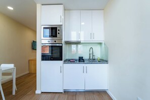 A compact kitchen with white cabinets, a built-in oven, and a microwave. - Close to Everything Your Oporto Gray PRM 2T (Porto)