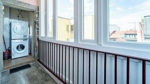 Ein Waschraum mit Waschmaschine und Trockner, ein Fenster mit Blick auf Gebäude und ein Heizkörper an der Wand.