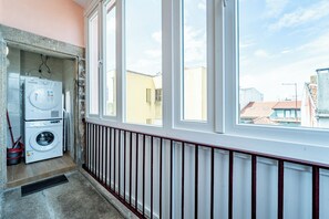 A laundry room with a washing machine and dryer, a window with a view of buildings, and a radiator along the wall. - Close to Everything Your Oporto Gray PRM 2T (Porto)