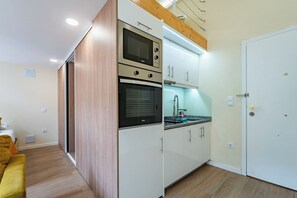 Eine kleine Küche mit integrierten Geräten, Holzboden und einer weißen Tür.
