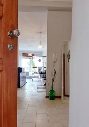 Een hal met een houten deur, een groene vaas en een eethoek met stoelen en een tafel.