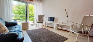 Een woonkamer met een bank, stoelen, een televisie en uitzicht op groen.