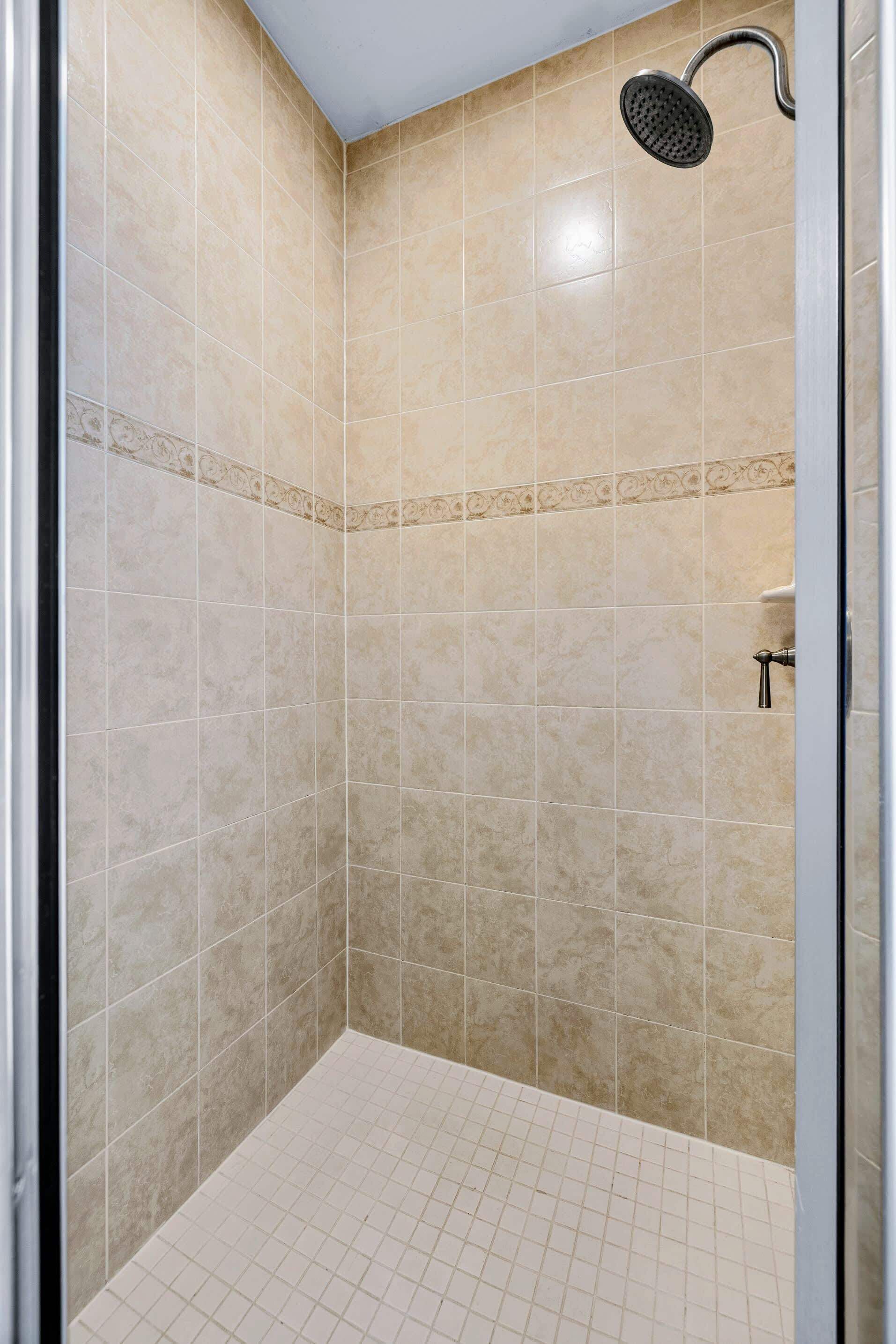 A shower with beige tiles, a showerhead, and a tiled floor.
