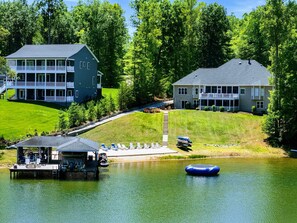 A lakeside property with a dock, a floating raft, and a large house with a porch.