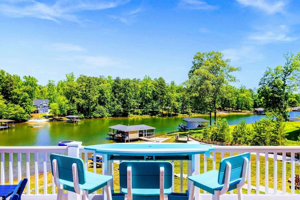 A lakeside deck with outdoor seating, a dock, and a house in the background.