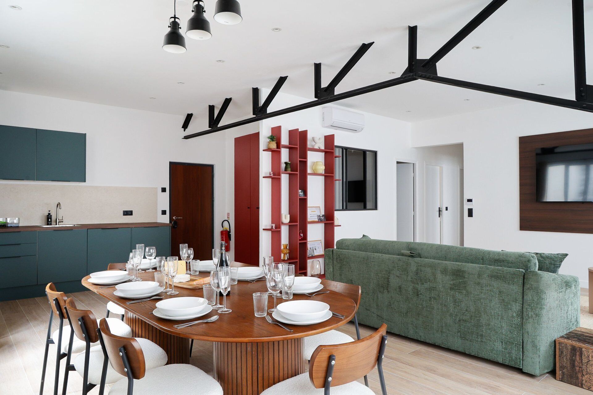 Una cocina moderna con zona de comedor, un sofá verde y un televisor montado en la pared.