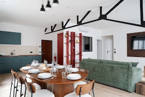 Une cuisine moderne avec un coin repas, un canapé vert et un téléviseur fixé au mur.