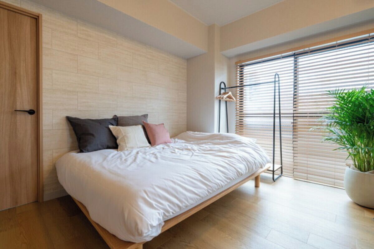 Un dormitorio moderno con una cama, una puerta de madera, una ventana con persianas y una planta en maceta.