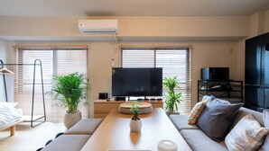 Ein modernes Wohnzimmer mit einer Couch, einem Couchtisch, einem Fernseher und zwei Blumentöpfen.