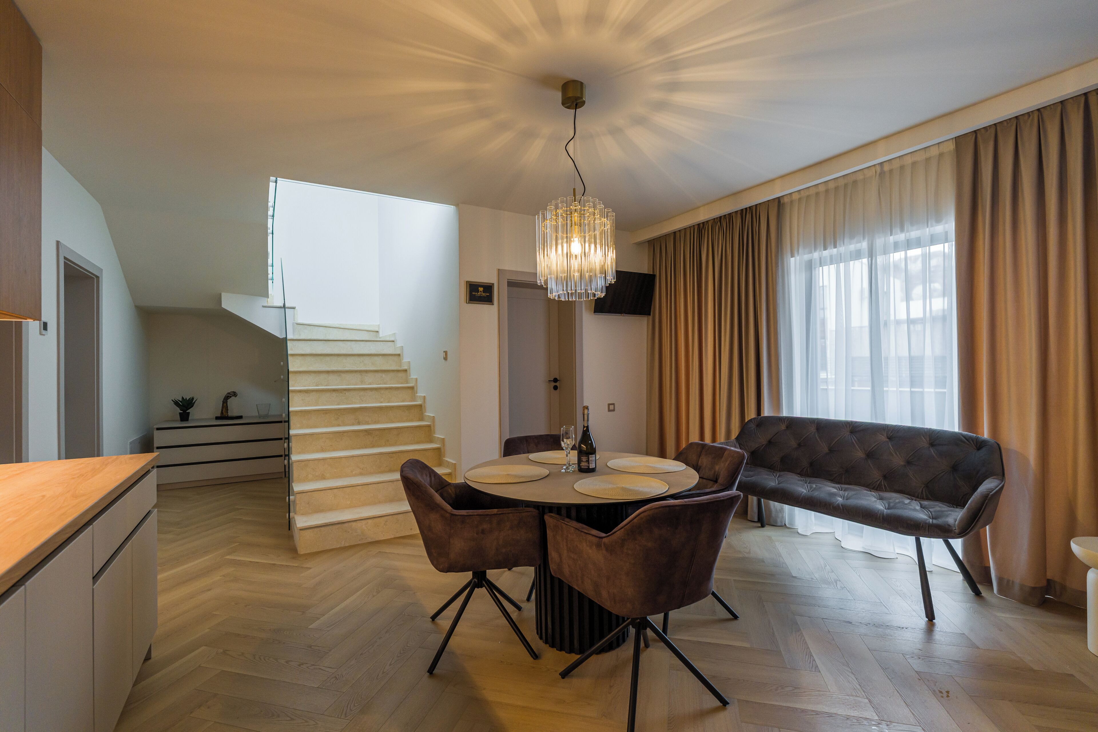 Un salon moderne comprenant une table à manger, des chaises, un canapé, un lustre et un escalier menant à l’étage supérieur.