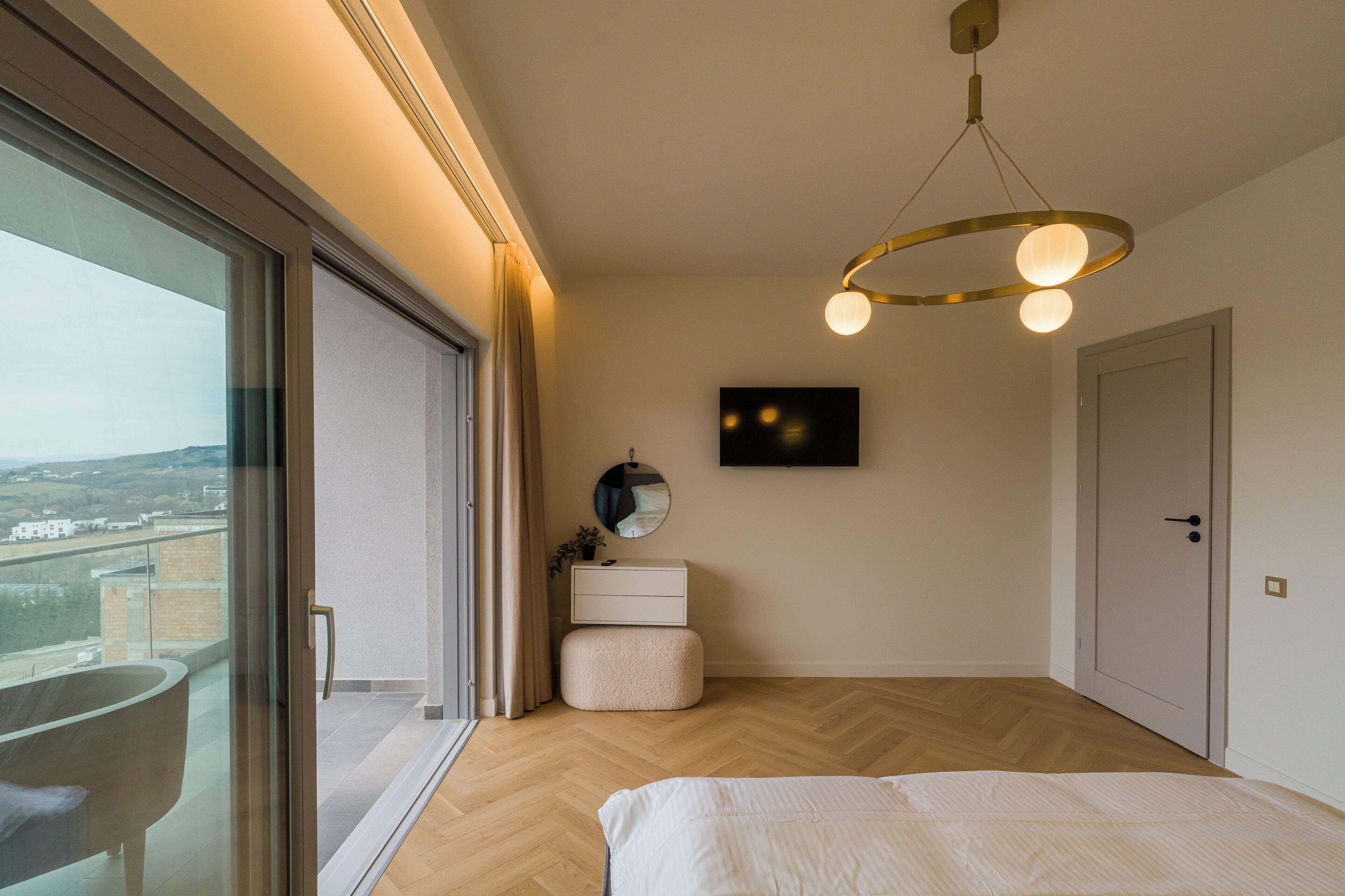 Une chambre avec une grande fenêtre, un lit, une table de chevet, un miroir et un téléviseur fixé au mur.